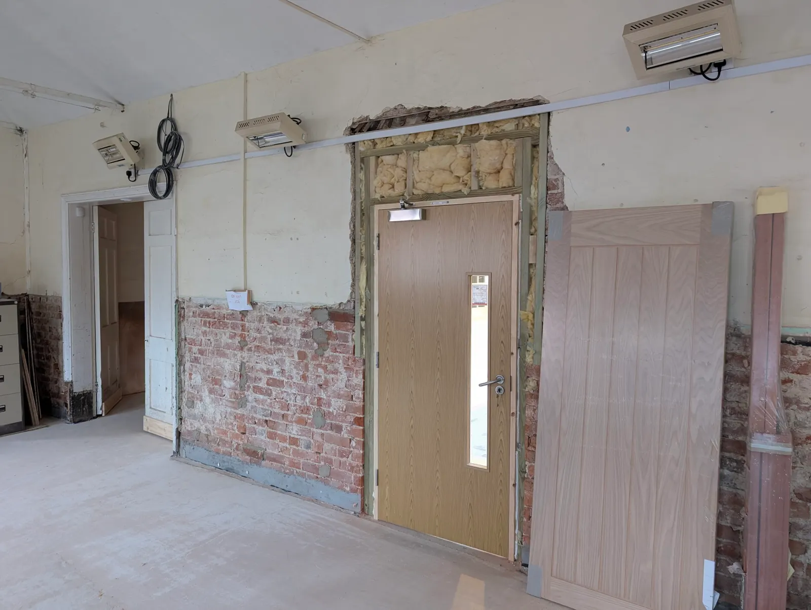 The new fire door fitted into the hall's exposed wall opening, ready for plastering